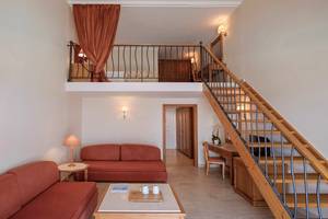 Innenansicht der Suite im Mitsis Family Village Beach Hotel mit Wohnzimmer, Schlafbereich und Treppe.