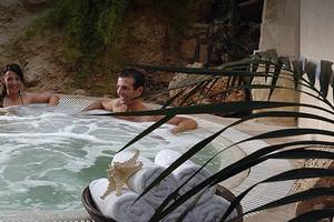 Ein Whirlpool im Freien mit zwei Personen im Coral Beach Hotel & Resorts, umgeben von Pflanzen und einem Tisch.