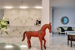 Lobby des Barceló Teguise Beach Adults Only Hotels mit Rezeption, rotem Pferdestatue und weißen Lilien im Glasvase.