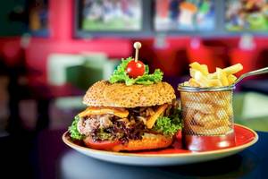 Ein Burger mit Salat, Tomaten und Pommes in einem Restaurant serviert.