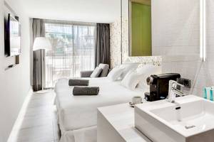 Ein modernes Hotelzimmer im Barceló Teguise Beach Adults Only mit weißem Bett, Schreibtisch, Lampen und Badezimmer