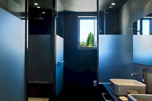 Badezimmer im Pelagos Suites Hotel & Spa mit blauen Fliesen, Dusche und offenem Fenster mit Gartenblick.