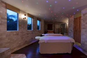 Massageraum im Iberostar Grand Paraiso Hotel mit zwei Massageliegen, farbigen Lichtern und Fenstern.