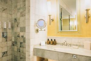 Badezimmer im Iberostar Grand Paraiso Hotel mit blauen Fliesen und gelben Wänden, einem Spiegel, Waschbecken und Duschbereich.