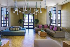 Lobby des Club Plimmiri Hotels mit modernen Möbeln, Holzboden und großen Fenstern.