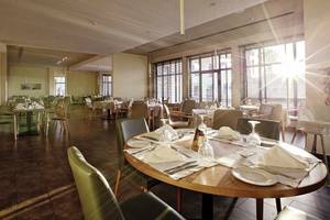 Innenansicht des Restaurants im Club Plimmiri Hotel mit runden Tischen, Stühlen und Sonnenlicht.
