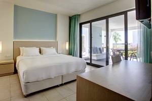 Innenansicht eines Hotelzimmers im Club Plimmiri Hotel mit Bett, Nachttischen und einer Terrasse davor.