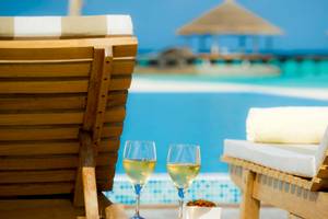 Zwei Lounge-Stühle mit Champagnergläsern am Pool mit Blick auf das Meer.