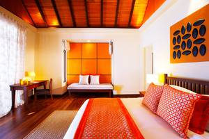 Innenansicht des Schlafzimmers im Kurumba Maldives Hotel mit Bett, Schreibtisch und Wanddekoration.