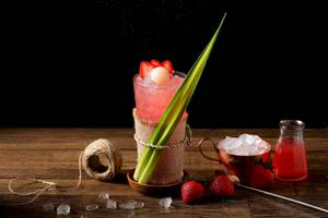 Ein roter Cocktail in einem Glas mit Eis und einer Strohhalm auf einem Holztisch.