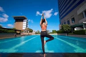 Frau praktiziert Yoga am Pool des Pathumwan Princess Hotels.