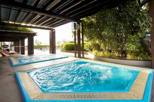 Zwei blaue Pools unter einem Dach im Pathumwan Princess Hotel mit Pflanzen und Sonnenliegen.
