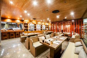 Innenbereich des Pathumwan Princess Hotels mit gepolsterten Sitzbänken, Holztischen und Bar.