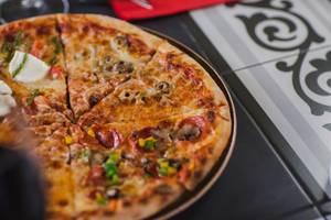 Eine Pizza mit diversen Belag, wie Peperoni, Zwiebeln und Pilzen, auf einem Tisch.