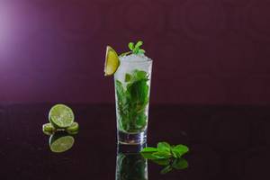 Cocktailglas mit Minze und Limette auf schwarzem Hintergrund
