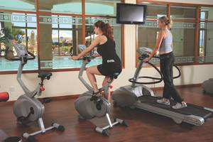 Zwei Frauen trainieren im Fitnesscenter des Alexander The Great Hotels auf einem Laufband und einem Fahrrad.