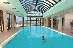 Eine Frau schwimmt im grünen Wasser des Innenpools des Alexander The Great Hotels.