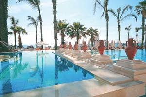 Außenpool des Alexander The Great Hotels mit blauem Wasser und roten Vasen.