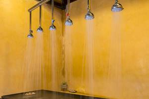 Ein Raum mit mehreren Duschköpfen, die Wasser sprühen, an einer gelben Wand.