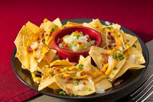 Ein Teller mit Nachos, überzogen mit Käse, Speck und Salsa, auf einem Tisch.