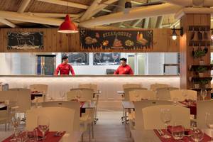Innenansicht der Steakhouse im H10 Conquistador Hotel mit Angestellten am Tresen und leeren Tischen.