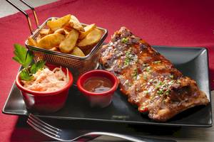 Gegrillte Rippchen mit Beilagen auf schwarzem Teller