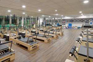 Fitnessstudio mit Pilates Reformer Geräten, großen Spiegeln und Holzboden.