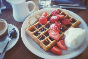 Ein Teller mit einer Waffel, Erdbeeren, Sahne und Kaffee.