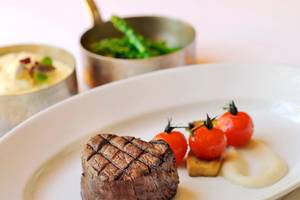Ein Steak auf einem weißen Teller im Park Hyatt Abu Dhabi Hotel & Villas, neben Tomaten und Beilagen.