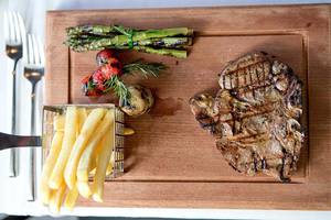 Ein Steak-Teller mit Pommes, Spargel, Tomaten und Rosmarin auf einem Holzbrett.