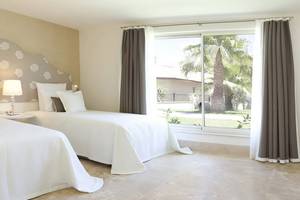 Zwei Betten im Zimmer des Paloma Oceana Hotels mit weißem Laken und Kissen, neben einem Fenster mit Blick auf einen Garten.