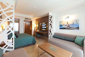 Interieur eines Hotelzimmers im Paloma Oceana Hotel mit einem Bett, Sofa, Tisch und Fernseher.
