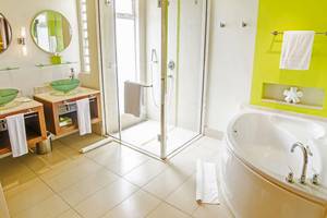 Badezimmer im Tamassa Bel Ombre Hotel mit zwei grünen Waschbecken, einer Duschkabine und einer Badewanne.