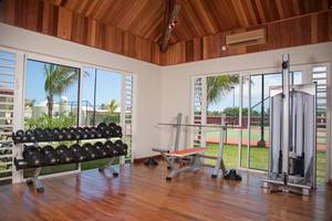 Fitnessraum im Hotel Tamassa Bel Ombre mit Geräten und Fenstern zum Tennisplatz.
