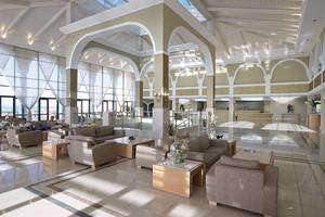 Innenansicht der Lobby des Porto Bello Royal Hotels mit großen Fenstern, heller Beleuchtung und modernen Möbeln.