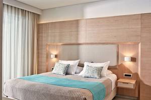 Ein modernes Hotelzimmer im Porto Bello Royal Hotel mit blauer Bettdecke und weißen Kissen.