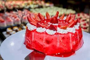 Ein roter Erdbeerkuchen auf einem weißen Teller im Hintergrund ein Buffet