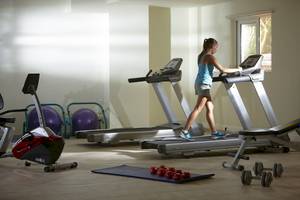 Ein Fitnessstudio im Astir Beach Hotel auf Kreta mit einer Frau, die auf einem Laufband läuft.