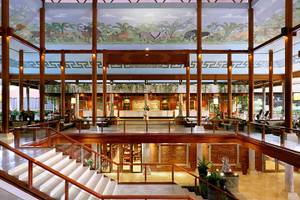 Innenansicht der Lobby des Melia Bali Hotels mit üppigen Wandmalereien und Holzsäulen.