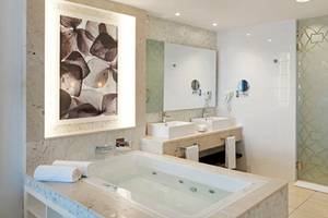Ein Badezimmer im Iberostar Origin Bella Vista Varadero Hotel mit einer Badewanne, zwei Waschbecken, einer Glasdusche und einem Kunstwerk.