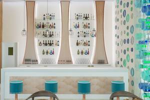 Innenansicht der Bar im Coral Level at Iberostar Selection Bávaro mit weißen Theken, Holzelementen und blauen Kreisen an der Wand.