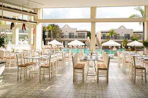 Poolseitiges Restaurant im Louis Paphos Breeze Hotel mit weißen Tischen und Stühlen unter Sonnenschirmen.