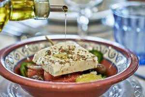 Olivenöl wird auf einen griechischen Salat in einer Schüssel gegossen.