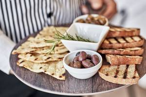 Eine Holzplatte mit Brot, Oliven, Rosmarin und gegrillten Beilagen.