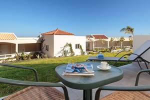Außenbereich des Rodos Princess Beach Hotels mit Garten, Liegestühlen und Gebäuden im Hintergrund.