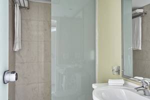 Badezimmer im Esperides Beach Resort mit Glasdusche, Waschbecken und Spiegel.