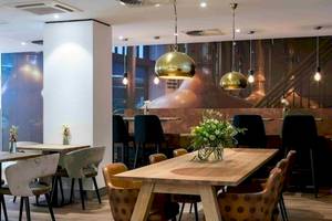 Innenansicht des Restaurants im NH Amsterdam Centre mit Holztischen, Stühlen und Kupferlampen.