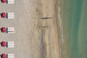 Luftaufnahme eines Luxushotels am Strand mit roten Sonnenschirmen und einer Person, die ins Wasser geht.