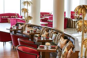 Innenbereich des Grecotel Lux Me Dama Dama Hotels mit roten Möbeln und goldenen Palmen.
