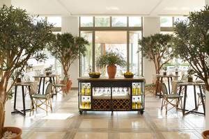 Innenbereich des Restaurants im Grecotel Lux Me Dama Dama mit großen Bäumen, Tischen und Stühlen.